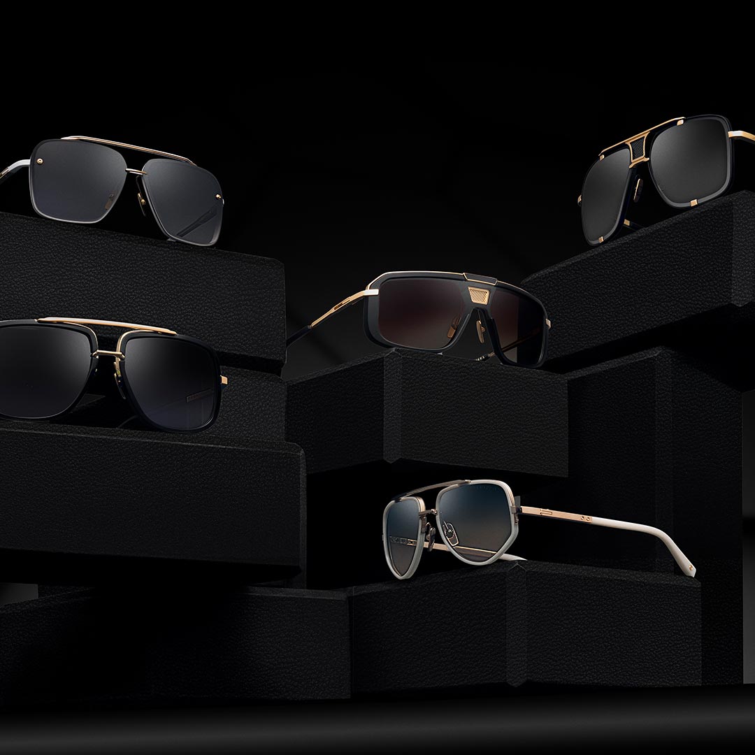A set of luxury sunglasses with black frames and gold accents are displayed on textured black pedestals against a dark background, conveying elegance.