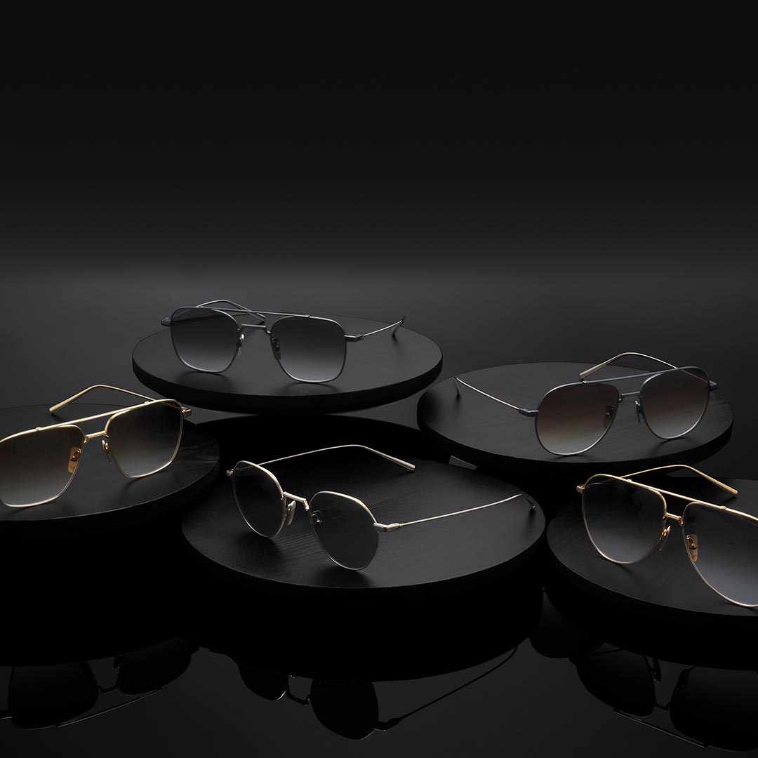 Elegant sunglasses displayed on black circular platforms against a dark background. The styles feature various sleek metal frames, exuding sophistication.