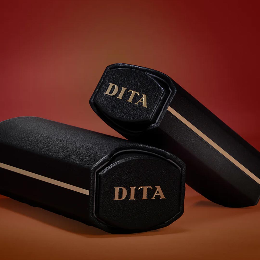 Two black hexagonal cases with "DITA" in gold lettering are positioned against a rich red gradient background, conveying elegance and luxury.