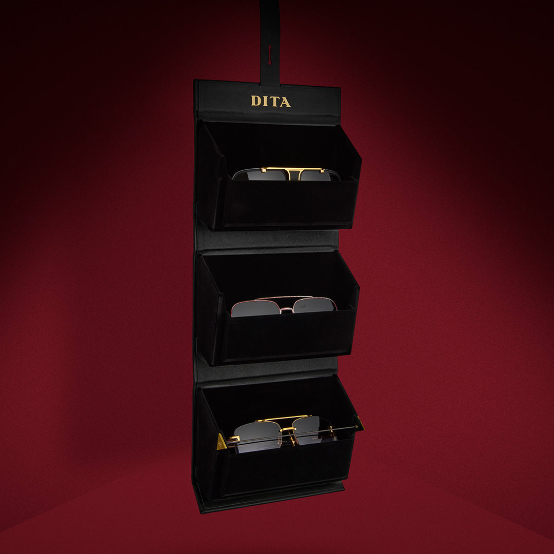 Two black hexagonal cases with "DITA" in gold lettering are positioned against a rich red gradient background, conveying elegance and luxury.