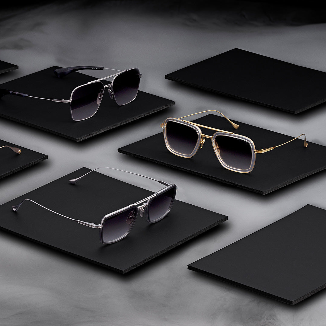 Sunglasses on black panels in a moody, sophisticated setting. Diverse styles with metallic frames and gradient lenses convey elegance and luxury.