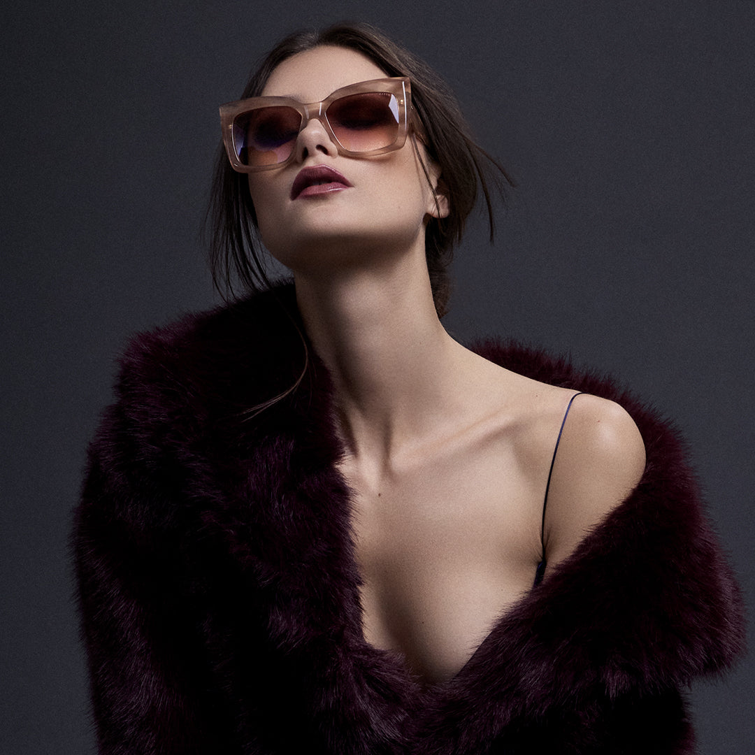 A woman with long blonde hair and glasses sits against dark, twisted wood. She wears a jeweled top and a white garment, conveying a serene, ethereal mood.