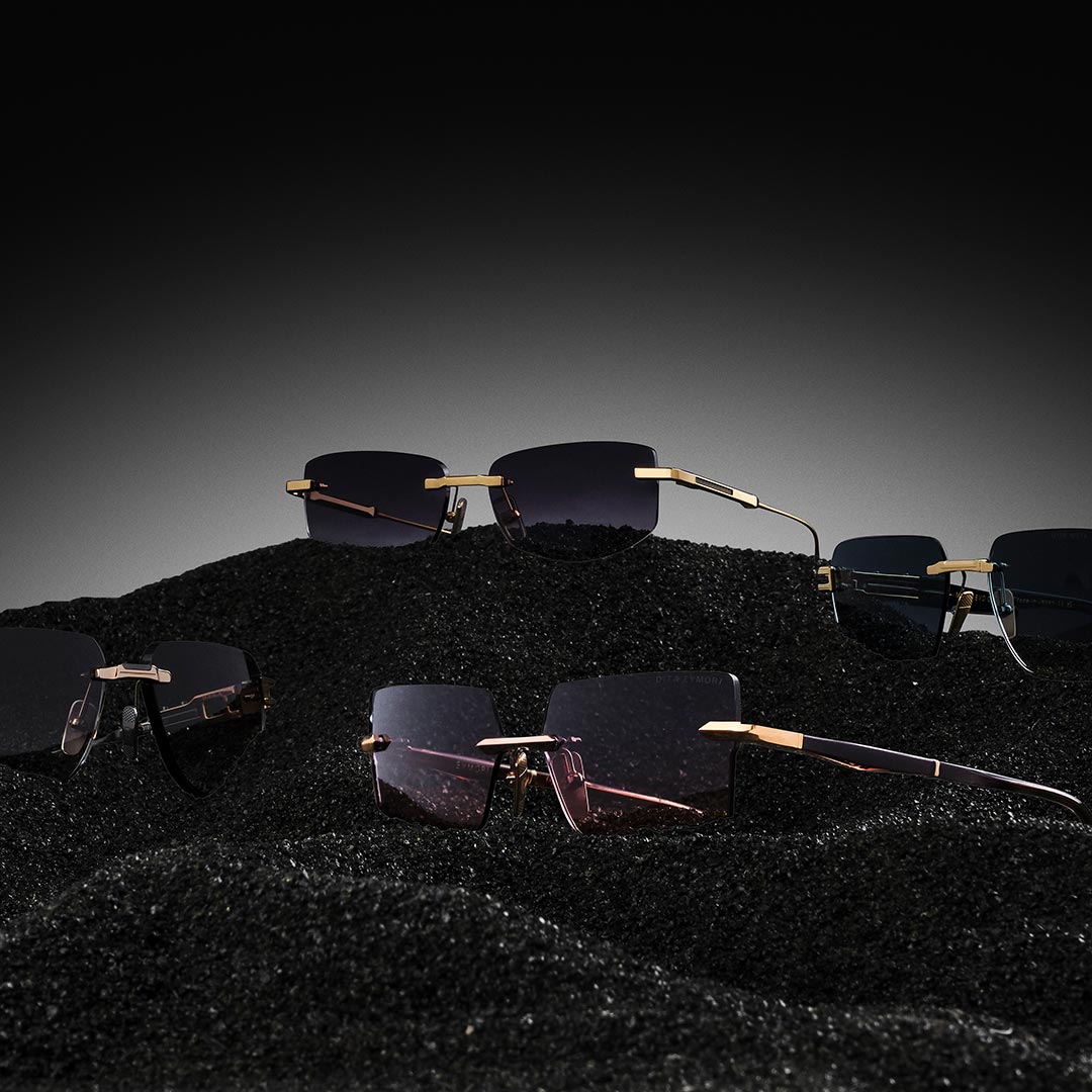Luxurious sunglasses with gold arms rest on textured black sand against a subtle gradient background, conveying elegance and modernity.