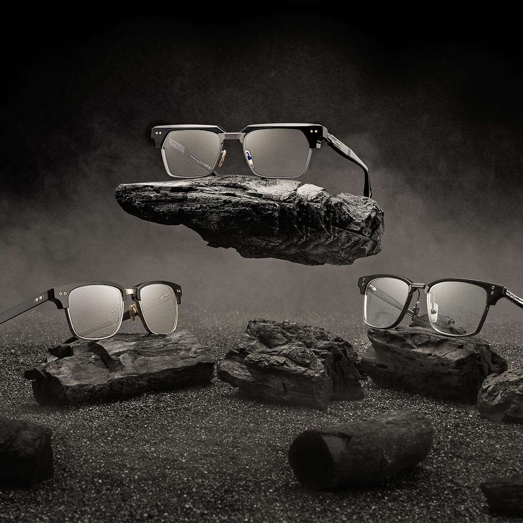 Three pairs of sunglasses with reflective lenses rest on dark, floating rocks against a moody, smoky backdrop, creating a futuristic and stylish scene.