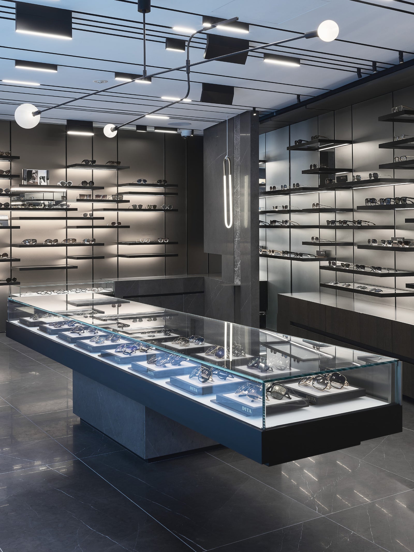 Modern eyewear store with sleek, minimalist design. Glass display cases and wall shelves showcase various eyeglasses and sunglasses. Bright, ambient lighting creates a stylish, inviting atmosphere.
