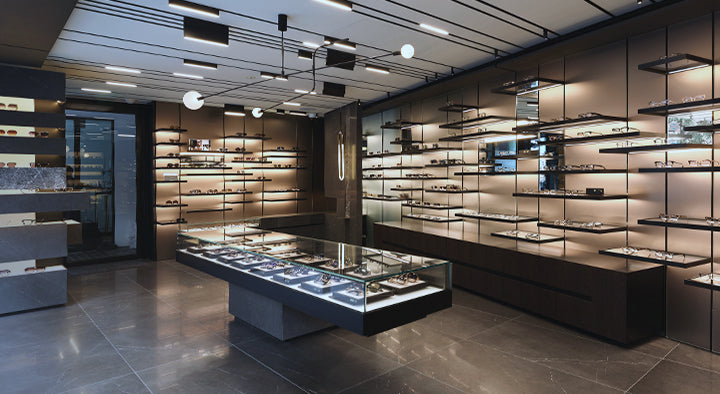 Modern eyewear store with sleek displays on walls and an illuminated central glass table showcasing glasses. The atmosphere is sophisticated and elegant.