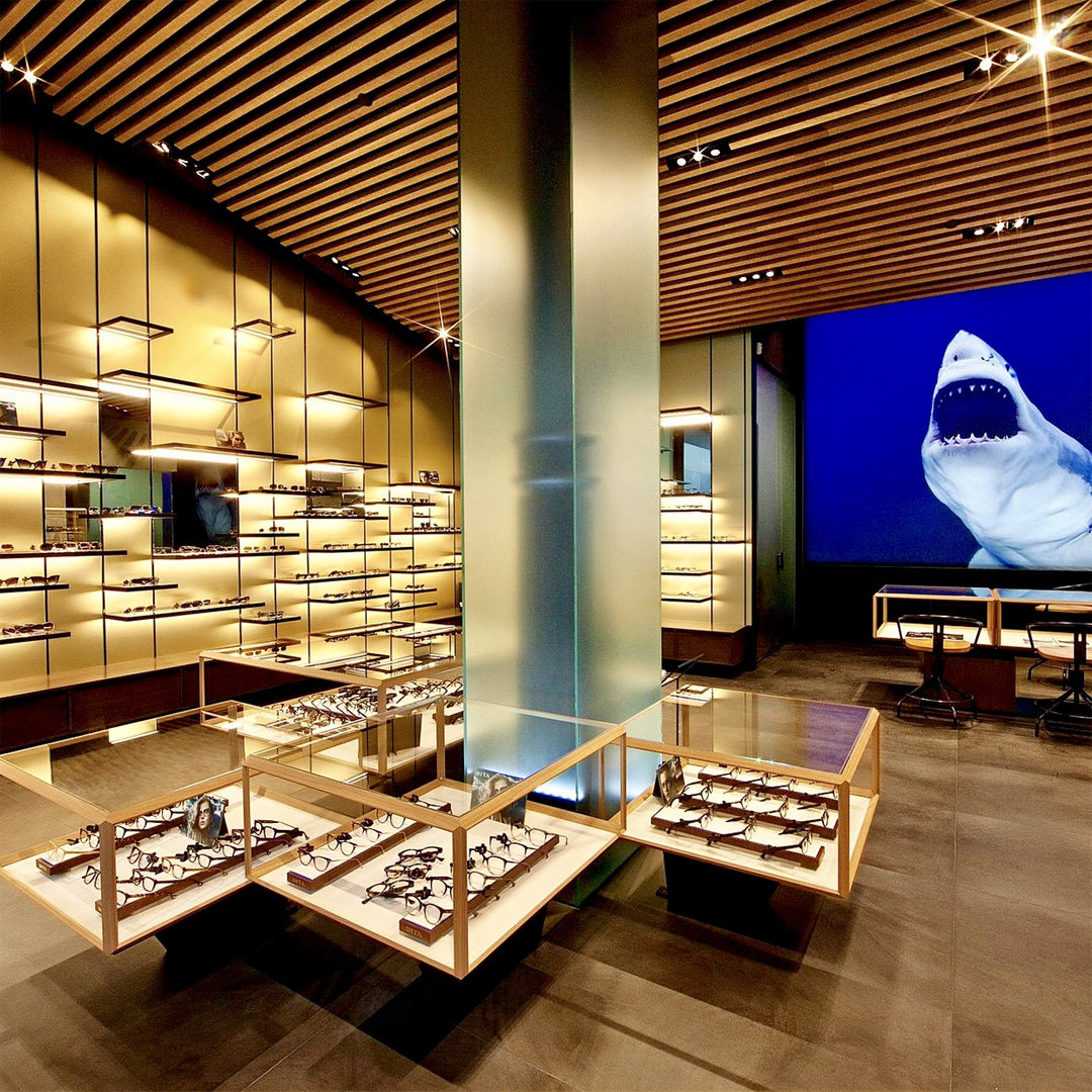 Modern eyewear store with sleek wooden shelves displaying glasses. A large screen shows an image of a shark, adding a bold, dramatic touch.