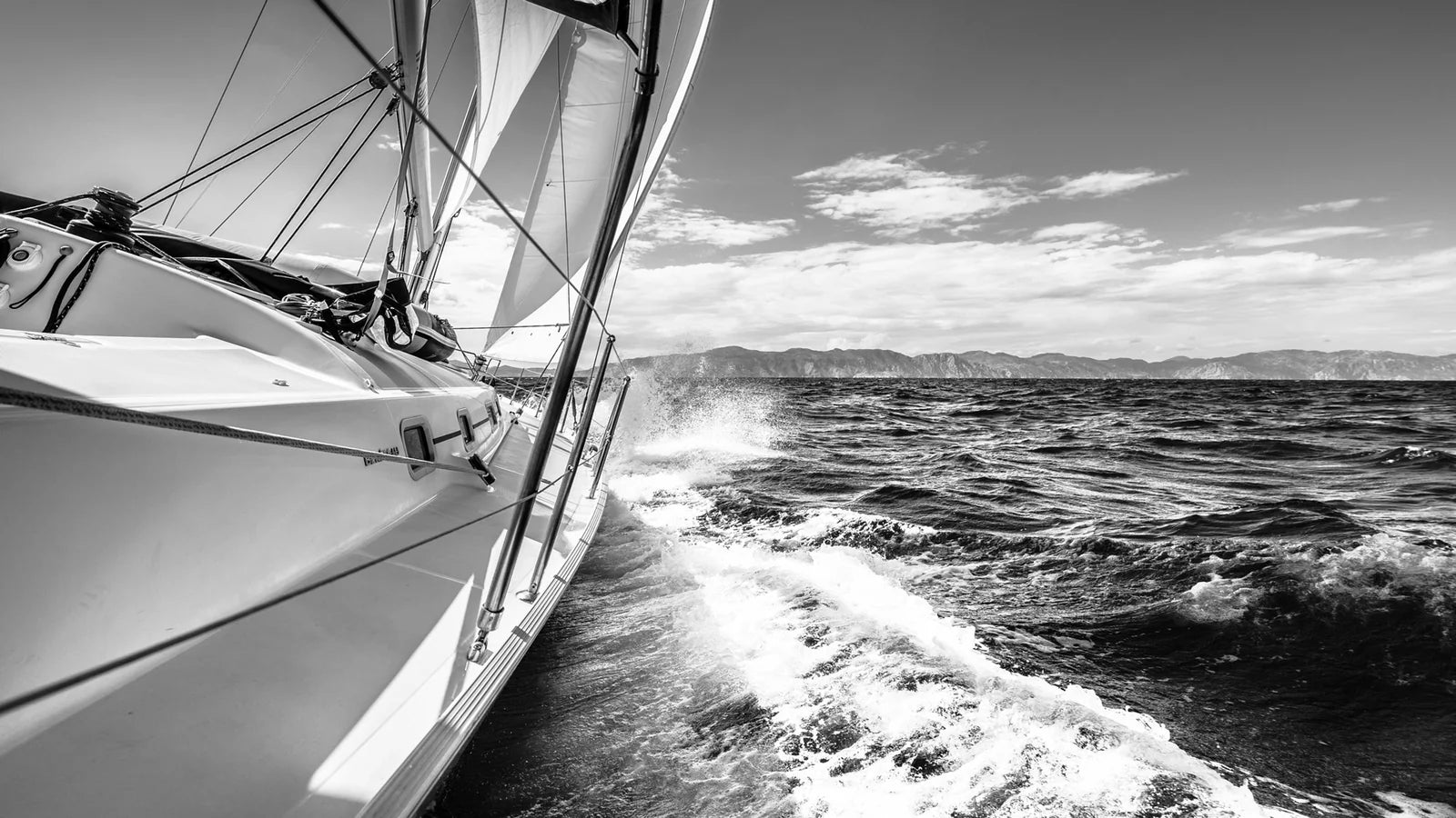 A sailboat glides through choppy waters under a clear sky, with waves splashing against the hull. Distant mountains create a serene backdrop.
