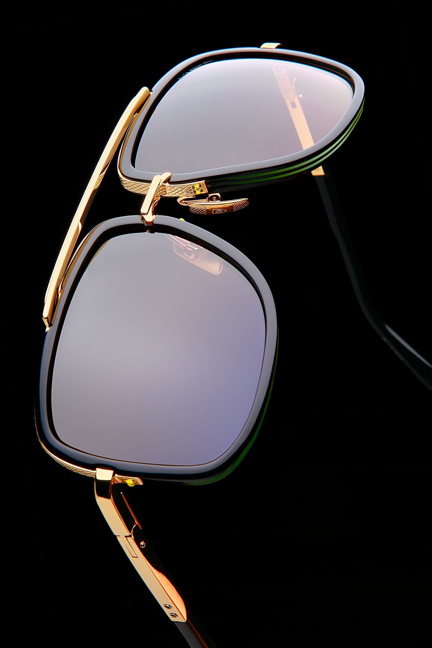 Elegant sunglasses with gold frames and dark lenses on a black background; the reflection creates a chic, sophisticated feel.