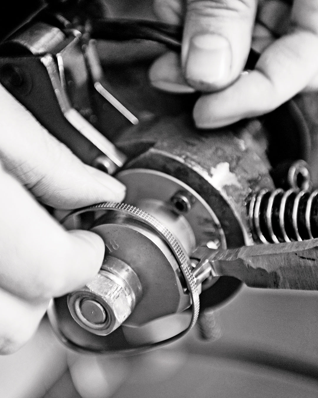 Close-up of hands adjusting camera gears in black and white. The detailed focus on mechanical components conveys precision and concentration.