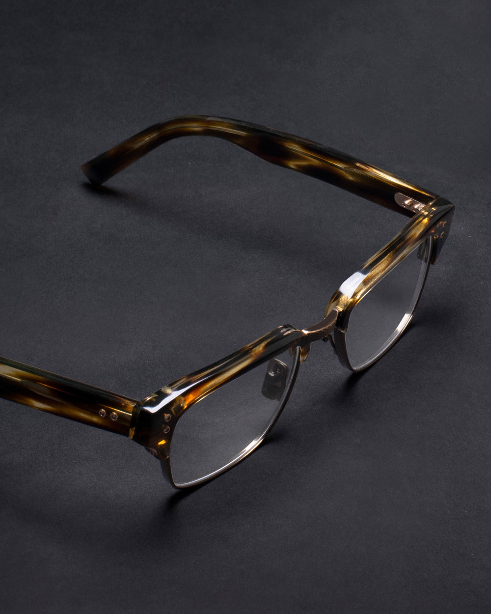 Tortoiseshell eyeglasses with square lenses on a dark surface. The stylish frame has a glossy finish, suggesting a modern and sophisticated look.