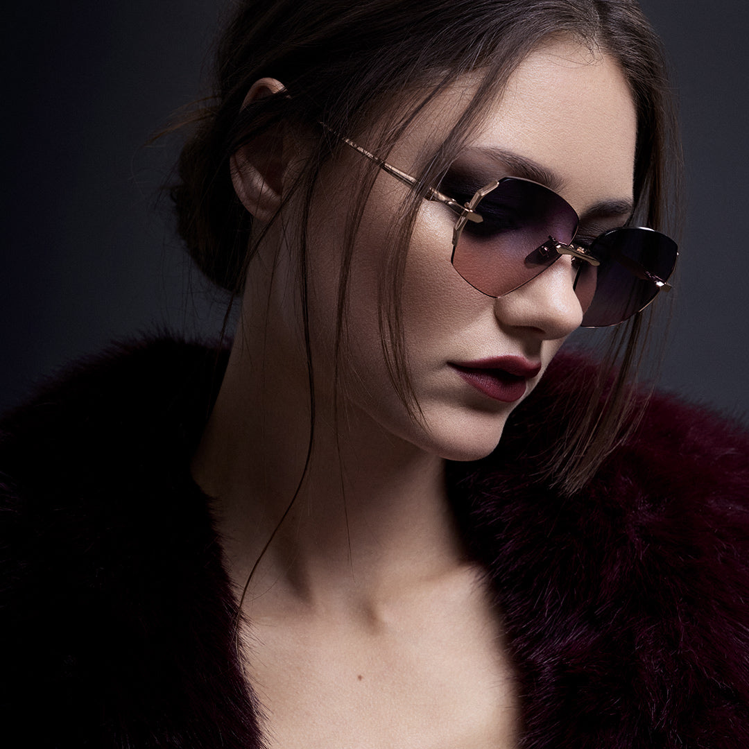 A woman with short, sleek hair and glasses poses confidently on a twisted tree trunk. She wears a low-cut, sleeveless outfit. The sky is dark and moody.